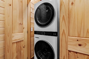 A front view of a modern, compact washer and dryer unit with a control panel, set against a wooden wall.