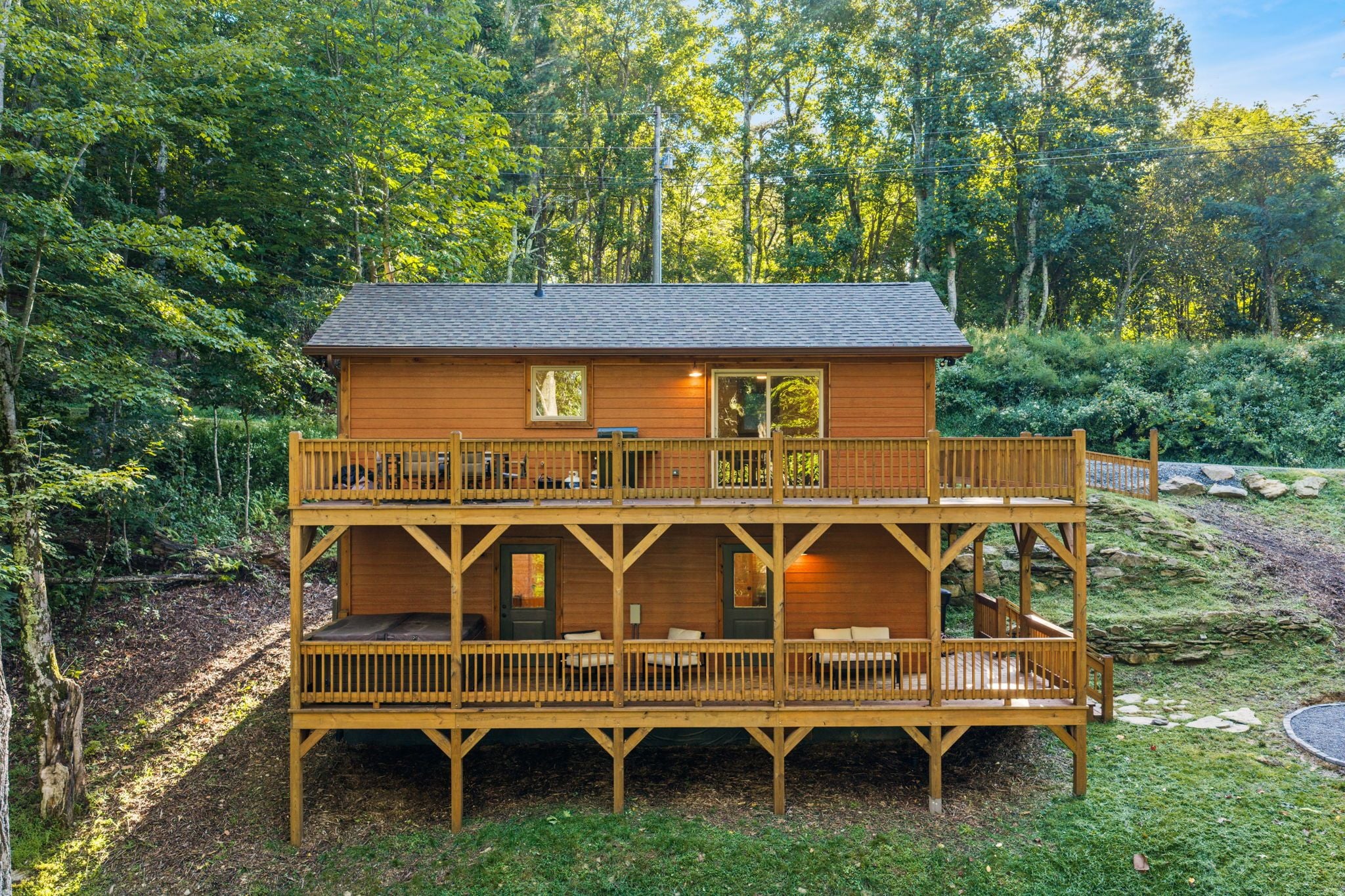 Une cabane en bois à deux étages, dotée d’un balcon et d’une terrasse, entourée de forêt.
