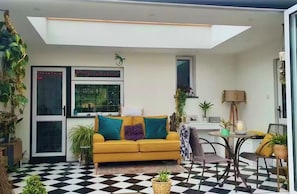 Un salon avec un canapé jaune, un sol à carreaux et une lucarne.