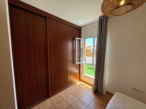 Ein Zimmer mit einer gleitenden Holztür, einem mit Vorhängen versehenen Fenster, einem Bett und einer Deckenleuchte.