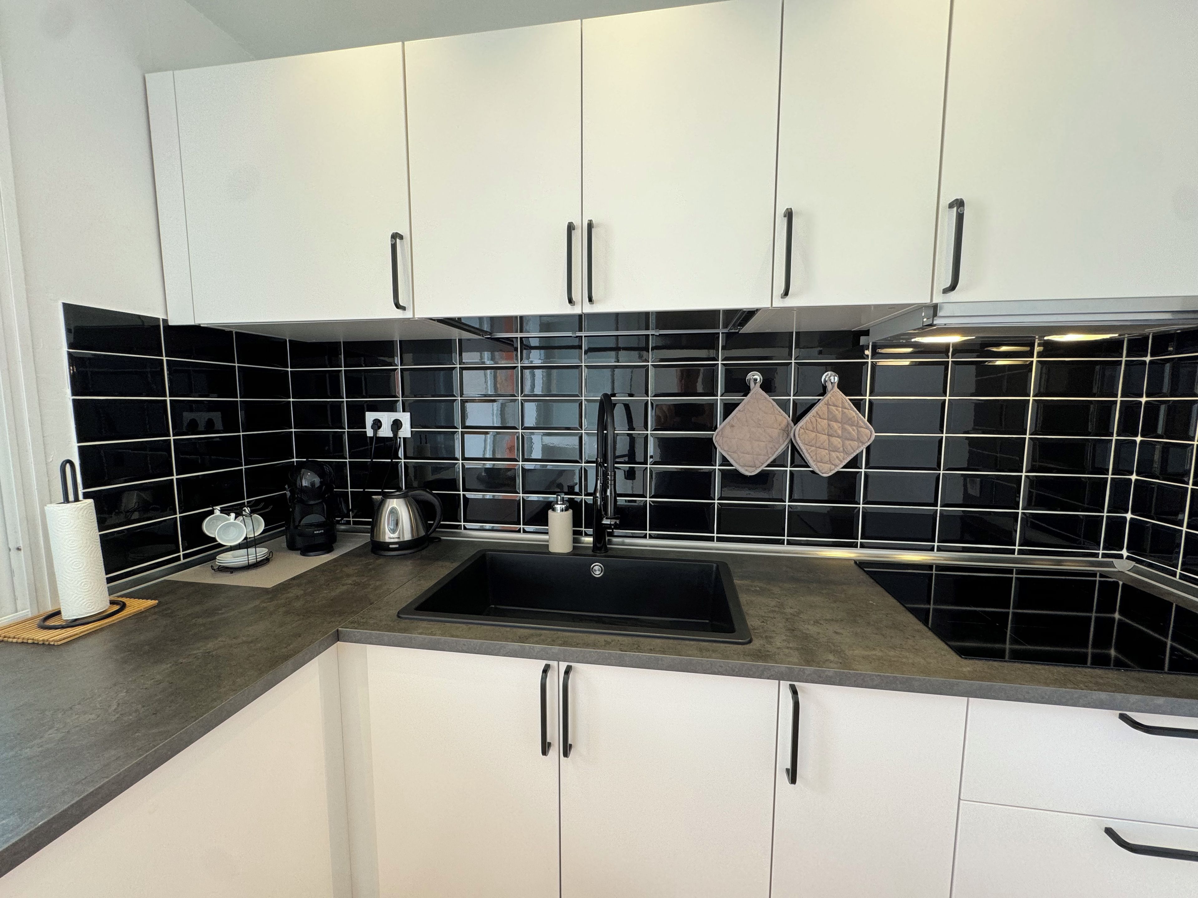 A modern kitchen with white cabinets, a black tiled backsplash, and a stainless steel sink.