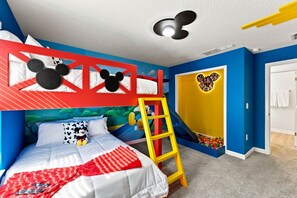 Een kinderkamer met een stapelbed, een ladder, een Mickey Mouse decoratie aan de muur en een bällebad.