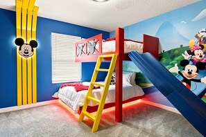 Ein Kinderzimmer mit einem Etagenbett, einer Leiter, einer Wanddekoration mit Mickey Mouse und einem Wandbild mit Disney-Figuren.