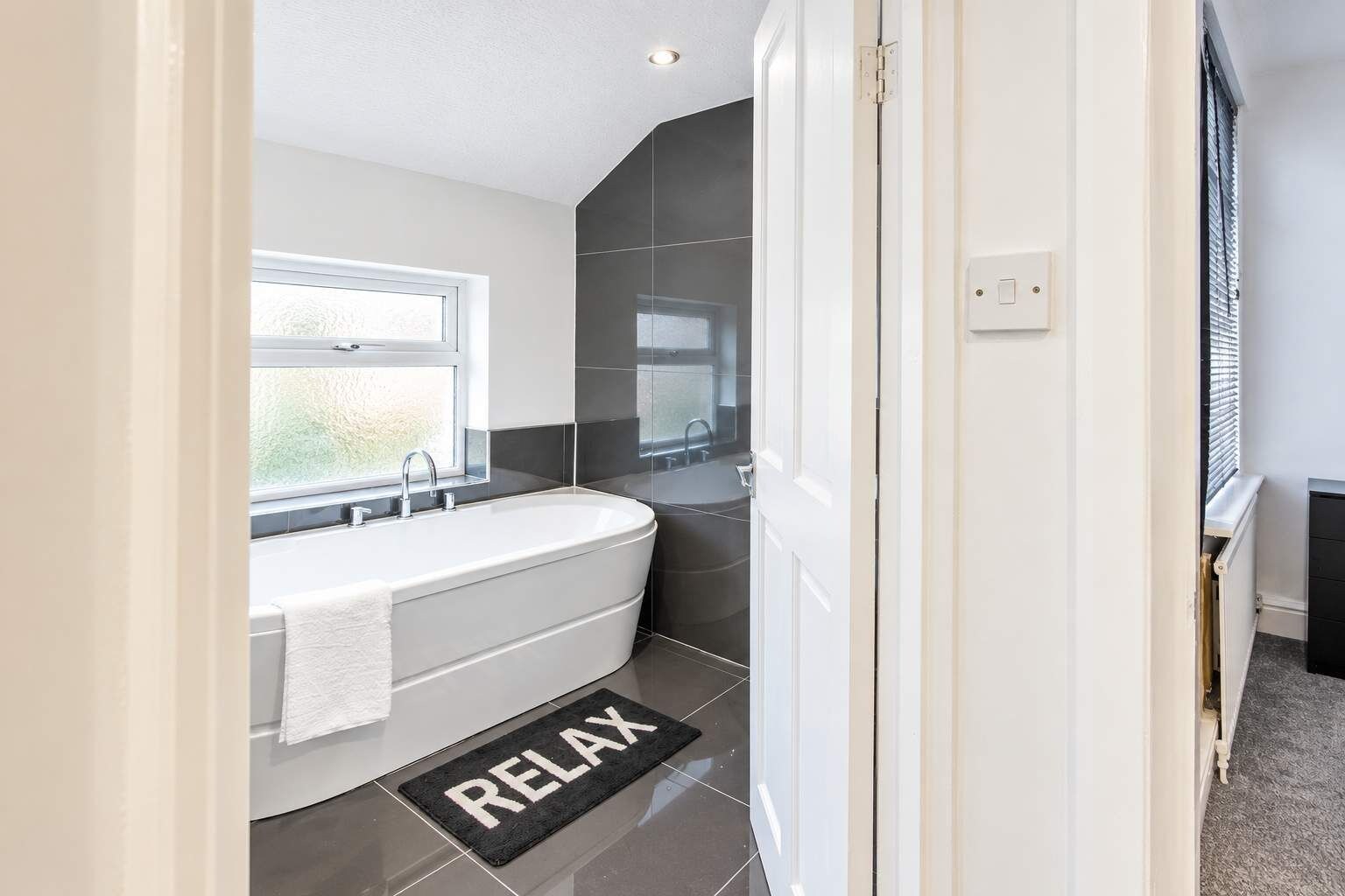 A modern bathroom with a freestanding bathtub, a window, and a 'RELAX' mat.
