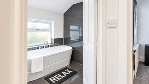 Une salle de bain moderne avec une baignoire sur pieds, une fenêtre et un tapis portant l’inscription « RELAX ».
