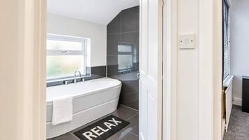 A modern bathroom with a freestanding bathtub, a window, and a 'RELAX' mat.