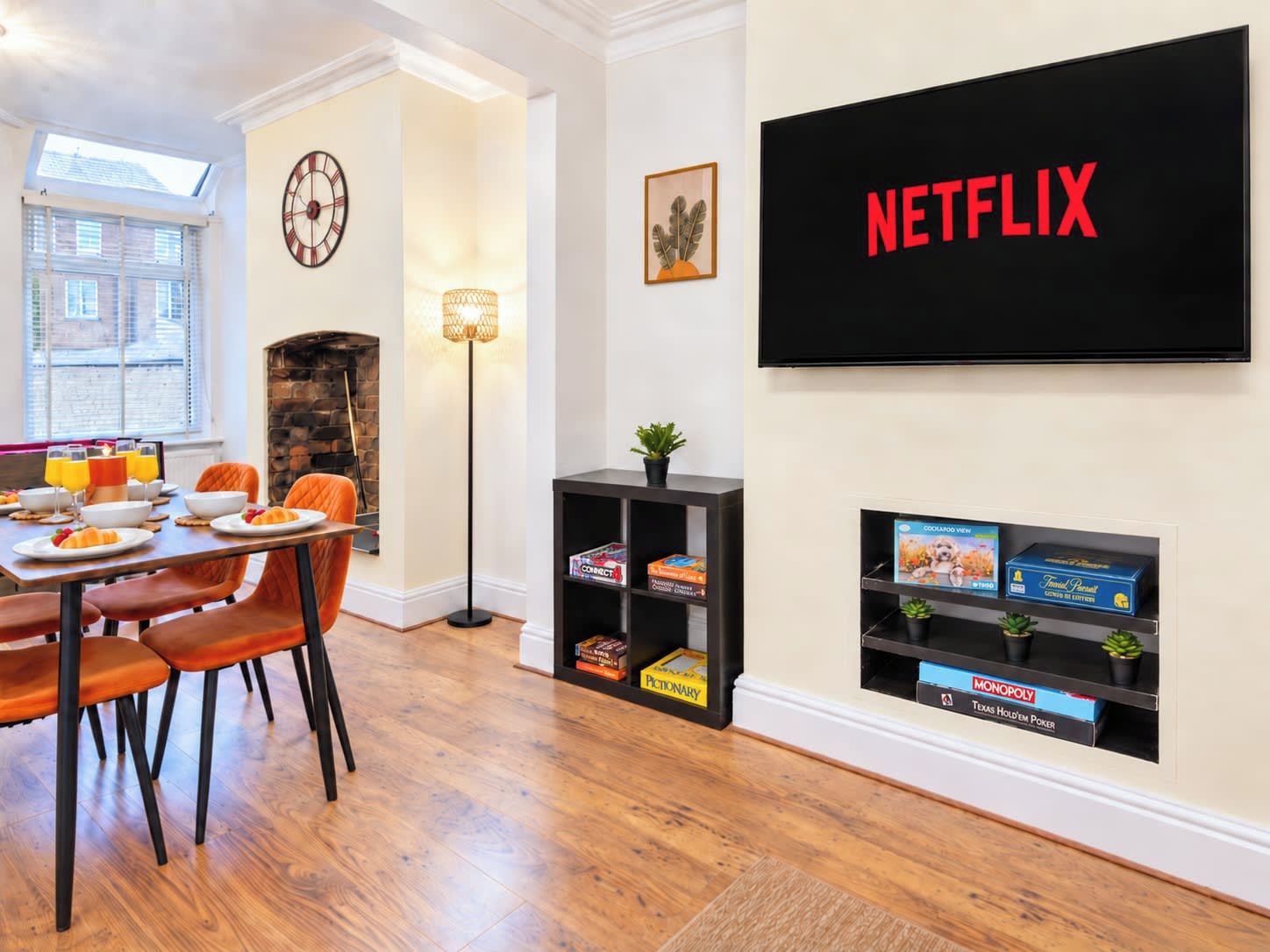 A modern living room with a dining area, a fireplace, a clock, and a wall-mounted TV displaying 'NETFLIX'.