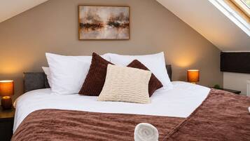A neatly made bed with a brown blanket and pillows, a painting on the wall, and a window providing natural light.