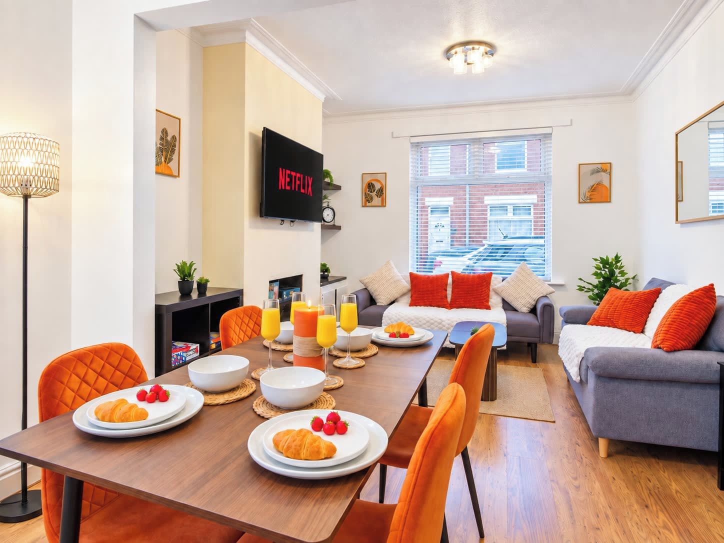 A modern living room with a dining area, a flat-screen TV, and a view of a building through large windows.