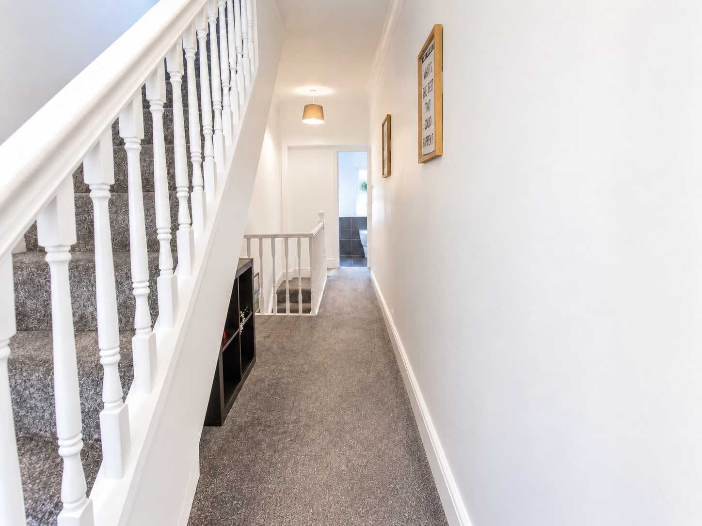 A hallway with a staircase on the left, a door at the end, and a wall-mounted light fixture.