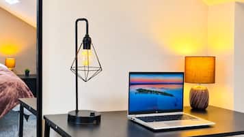 A laptop on a desk with a geometric lamp, a laptop stand, and a lamp with a textured lampshade.
