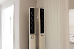 A white air conditioning unit with a digital display indicating 24 degrees Celsius, placed in a room with white walls and a window with blinds. - [SOYO] Serene 2-bedroom apartment with AC in vibrant Seoul (Mapo-gu)