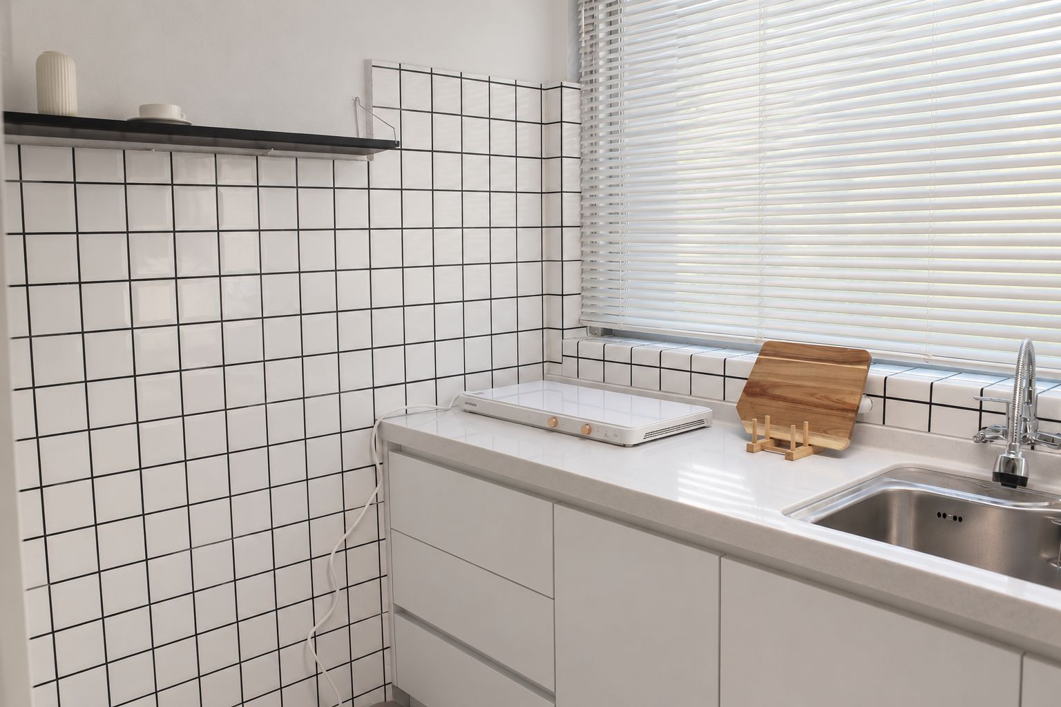 A kitchen with white subway tiles, a built-in oven, a sink with a faucet, and a window with blinds.