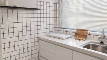 A kitchen with white subway tiles, a built-in oven, a sink with a faucet, and a window with blinds.
