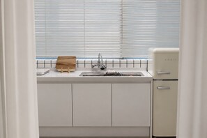 Eine Küche mit Spüle, Schneidebrett aus Holz und Kühlschrank in Weiß.