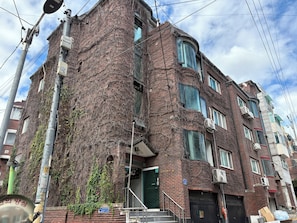 A multi-story brick building with a green door, visible staircases, and multiple windows. - [SOYO] Serene 2-bedroom apartment with AC in vibrant Seoul (Mapo-gu)