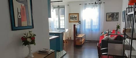 A spacious living area with a wooden floor, a dining table with chairs, a sofa, and a TV.