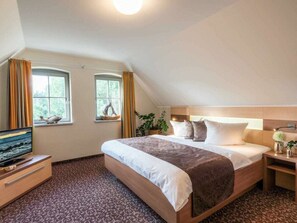 Ein Hotelzimmer mit einem Bett, einem Fernseher, zwei Fenstern, einer Pflanze und einer Lampe.