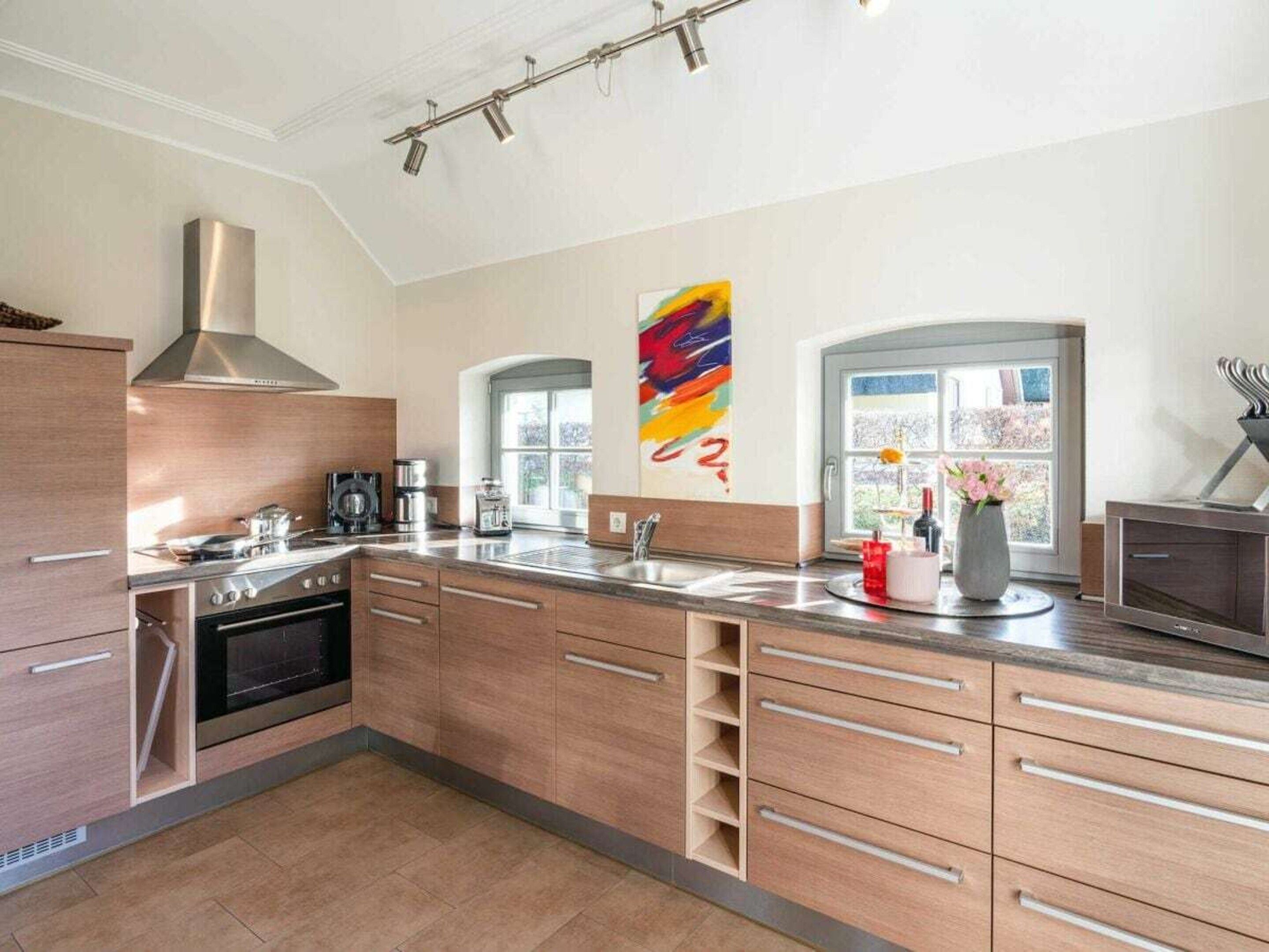 A modern kitchen with a stainless steel range hood, a large island with a sink, and a colorful abstract painting on the wall.