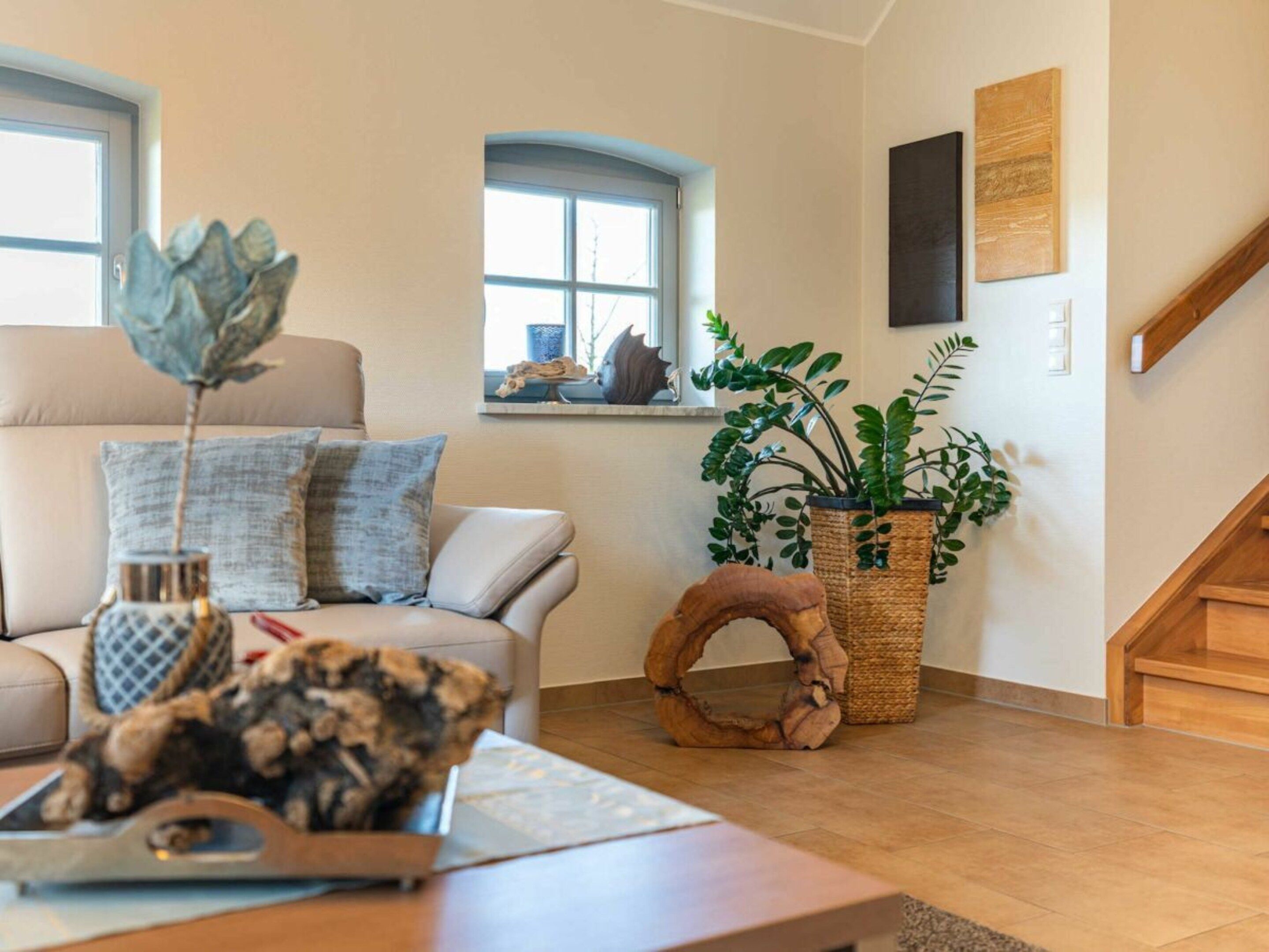 Un salon avec un canapé, une table basse, une plante en pot et un anneau décoratif en bois posé sur le sol.