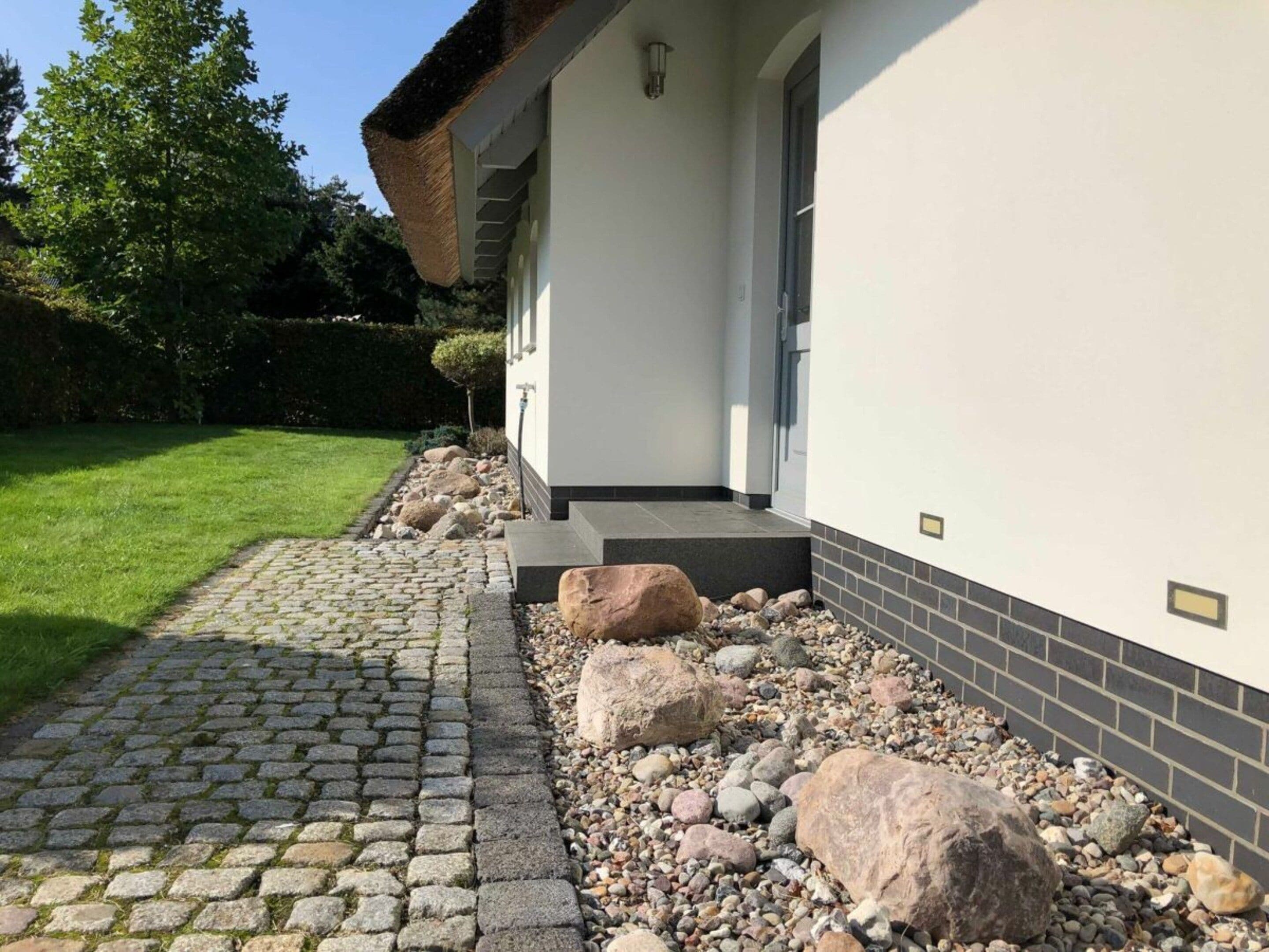 A modern building with a white exterior, a cobblestone pathway, and a garden area with rocks and a small tree.