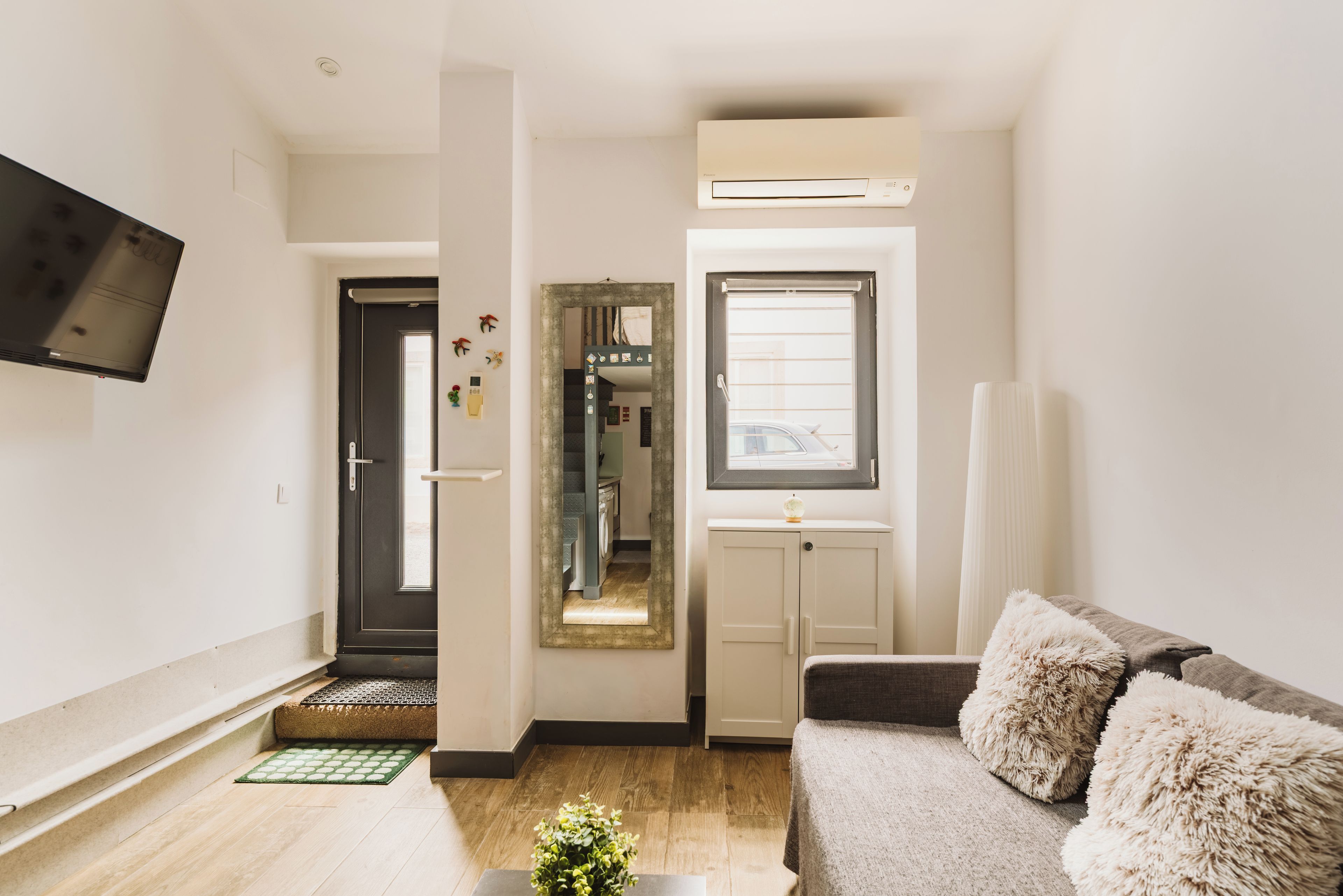 Una sala de estar con un sofá, un televisor, una puerta y una ventana.