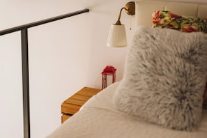 A bedroom with a bed, a nightstand, a lamp, and a red object on the nightstand. - Beautiful and cozy apartment in Belém. (Lisboa)