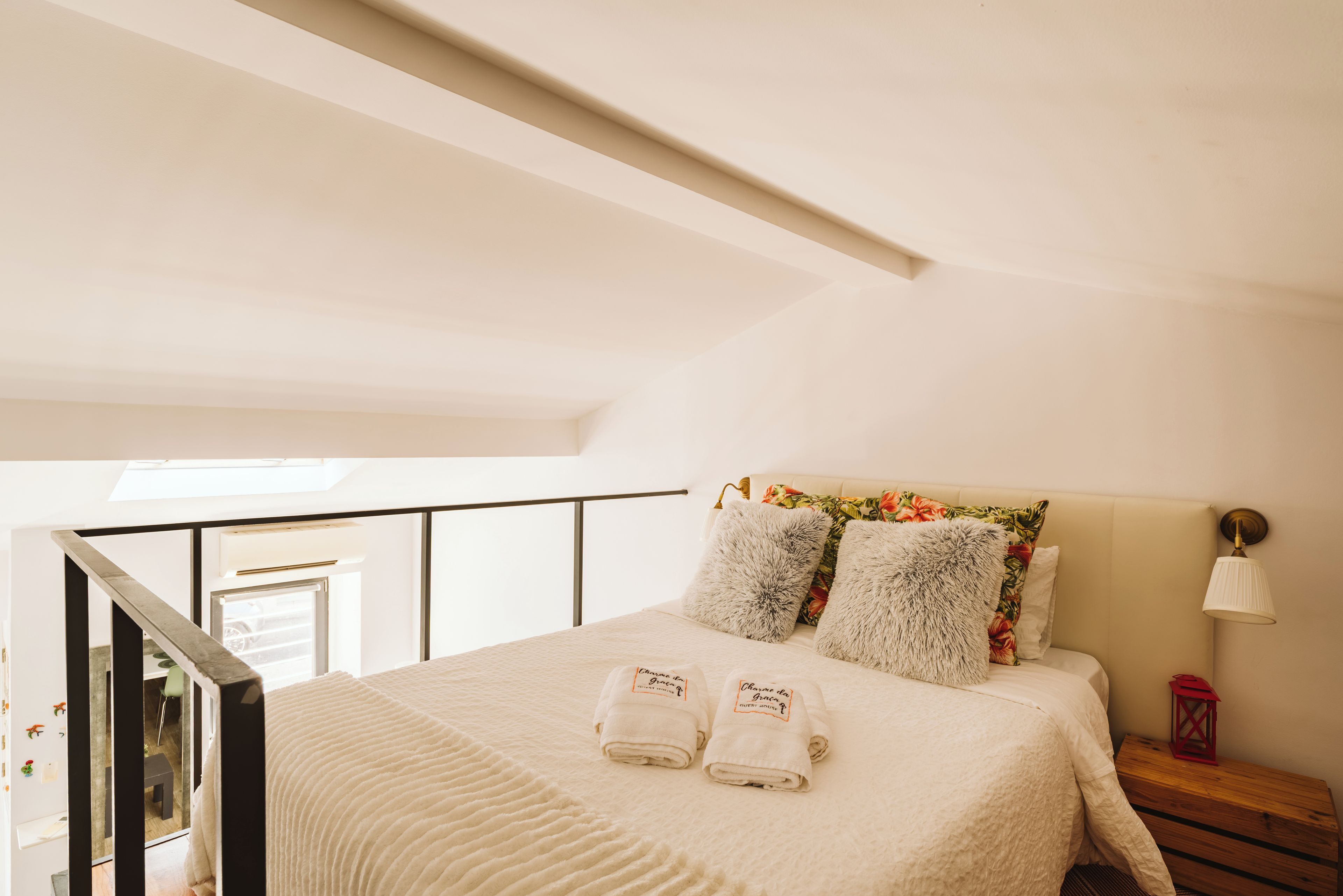 Une chambre à coucher avec un lit, des oreillers, une table de chevet, une lampe et une vue sur le balcon.