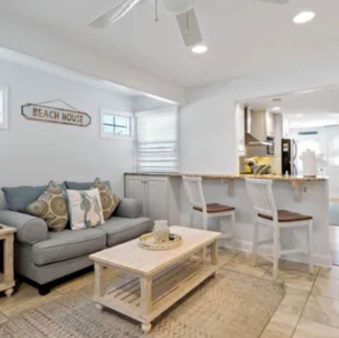 Ein modernes Wohnzimmer mit einer Couch, einem Couchtisch und einem Schild mit der Aufschrift 'BEACH HOUSE'.