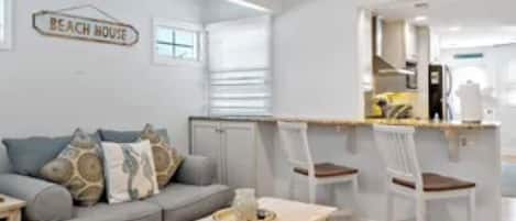 Ein modernes Wohnzimmer mit einer Couch, einem Couchtisch und einem Schild mit der Aufschrift 'BEACH HOUSE'.