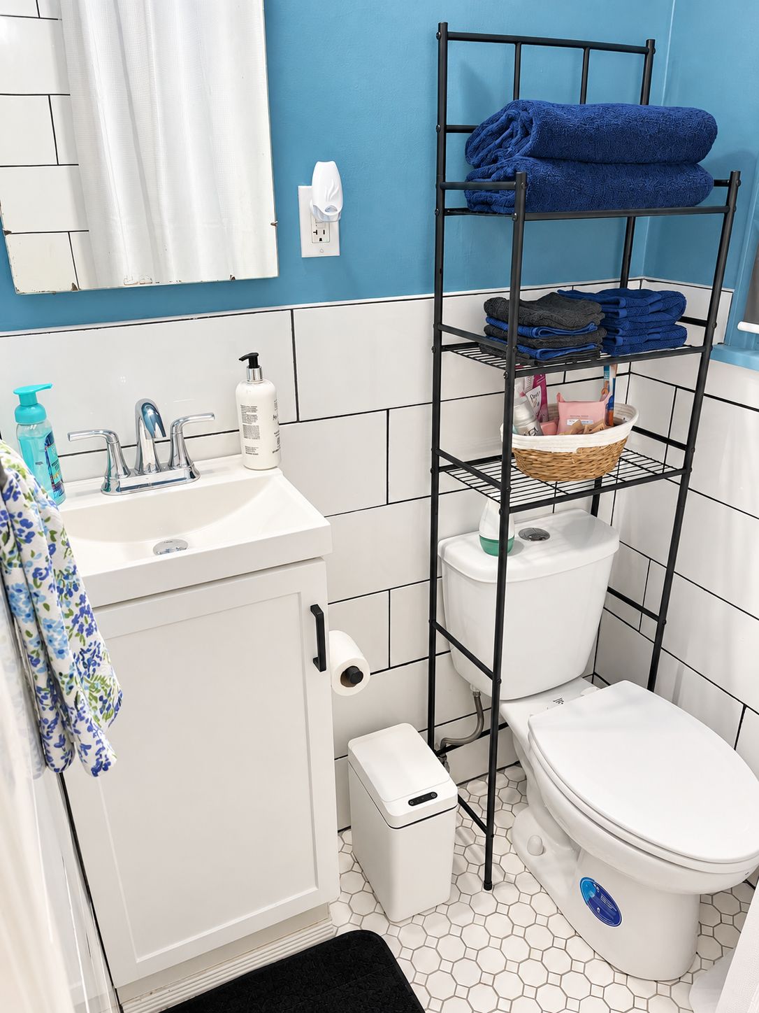 Un baño con un lavamanos blanco, un inodoro y un estante metálico negro con toallas.
