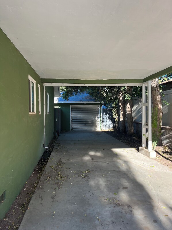 A covered outdoor area with a concrete floor, a garage door, and a green wall.