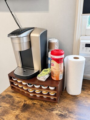 A coffee maker on a wooden stand with a paper towel and a coffee mug beside it.