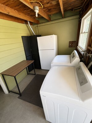 A compact laundry room with a washing machine, a dryer, a small table, and a window.