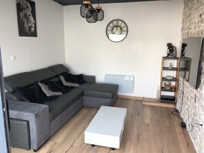A modern living room with a sectional sofa, a white coffee table, a TV, and a stone wall. - Maison de charme au coeur du village de l'Houmeau (L'Houmeau)