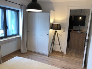 Et værelse med et stort vindue, en dør, en lampe på et stativ og et tekøkken med et fjernsyn.
