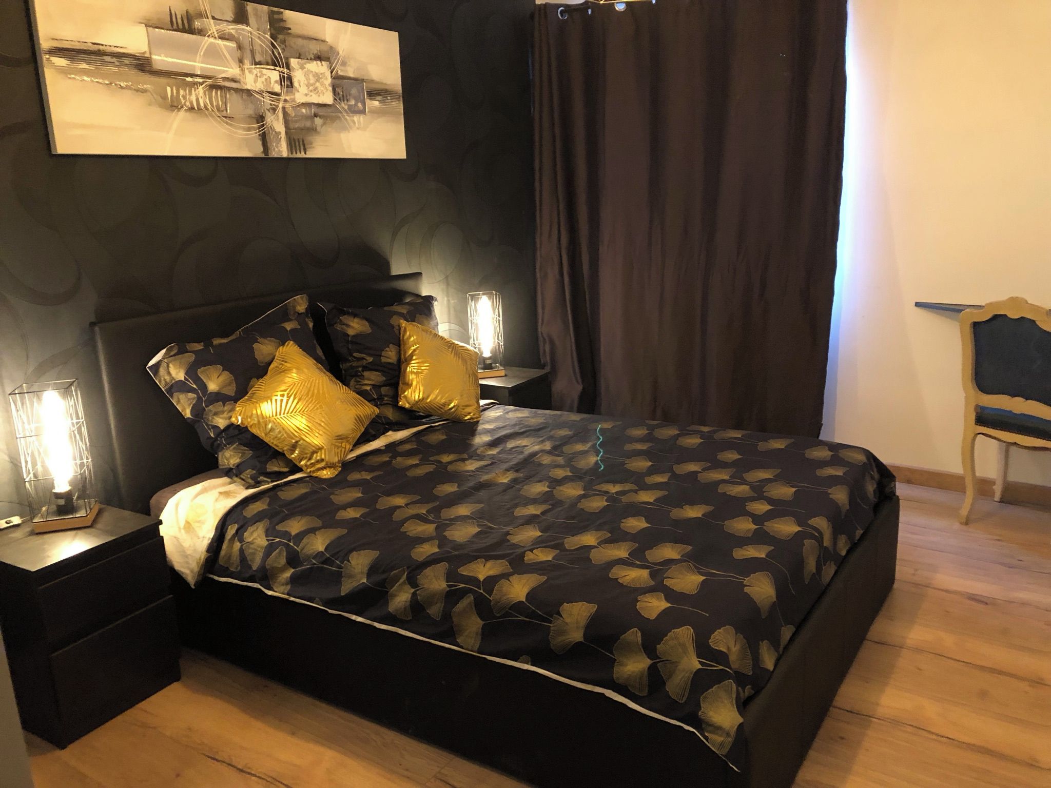 A bedroom with a bed, nightstands, a lamp, a chair, and a painting on the wall.