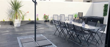 An outdoor patio with a dining table, chairs, a grill, and a large umbrella.