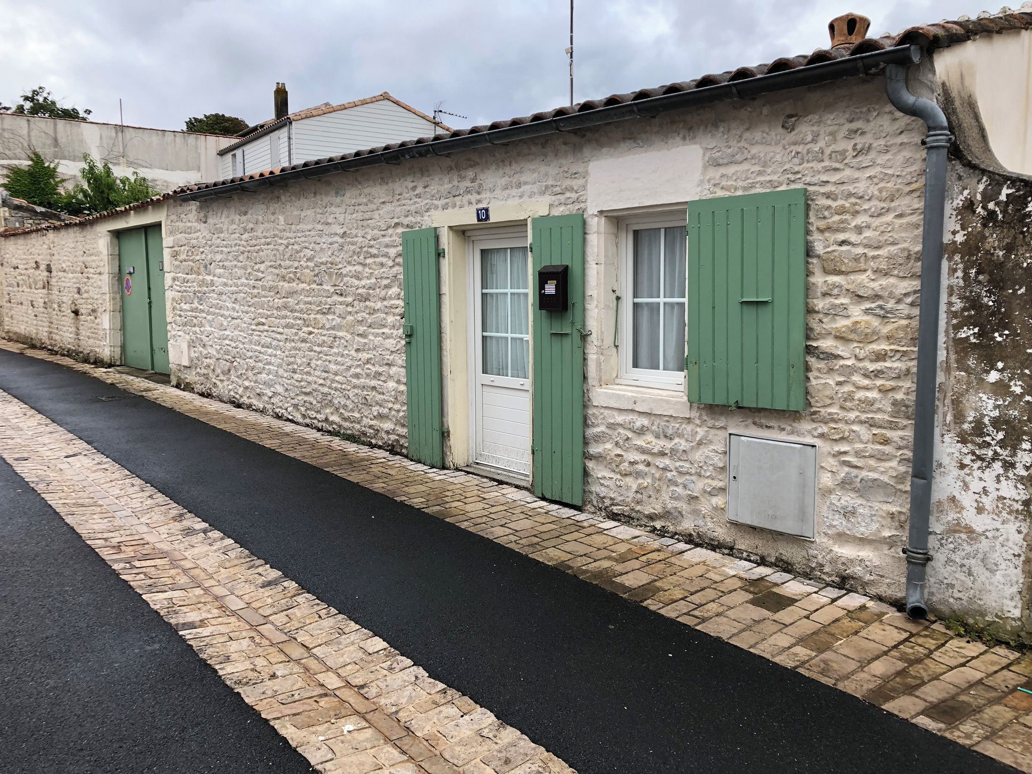 Un edificio de piedra con contraventanas verdes, una puerta y una ventana con buzón.