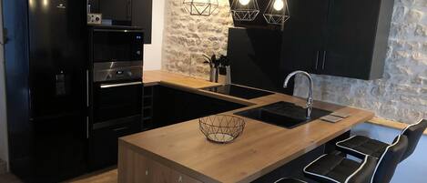 A modern kitchen with a central island, black cabinetry, a stone accent wall, and pendant lighting.
