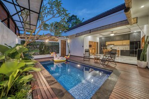 A swimming pool with a wooden deck, a dining area with chairs and a table, and a kitchen with modern appliances. - Stylish 3BR Pool Villa in Canggu, Bali (Bali)
