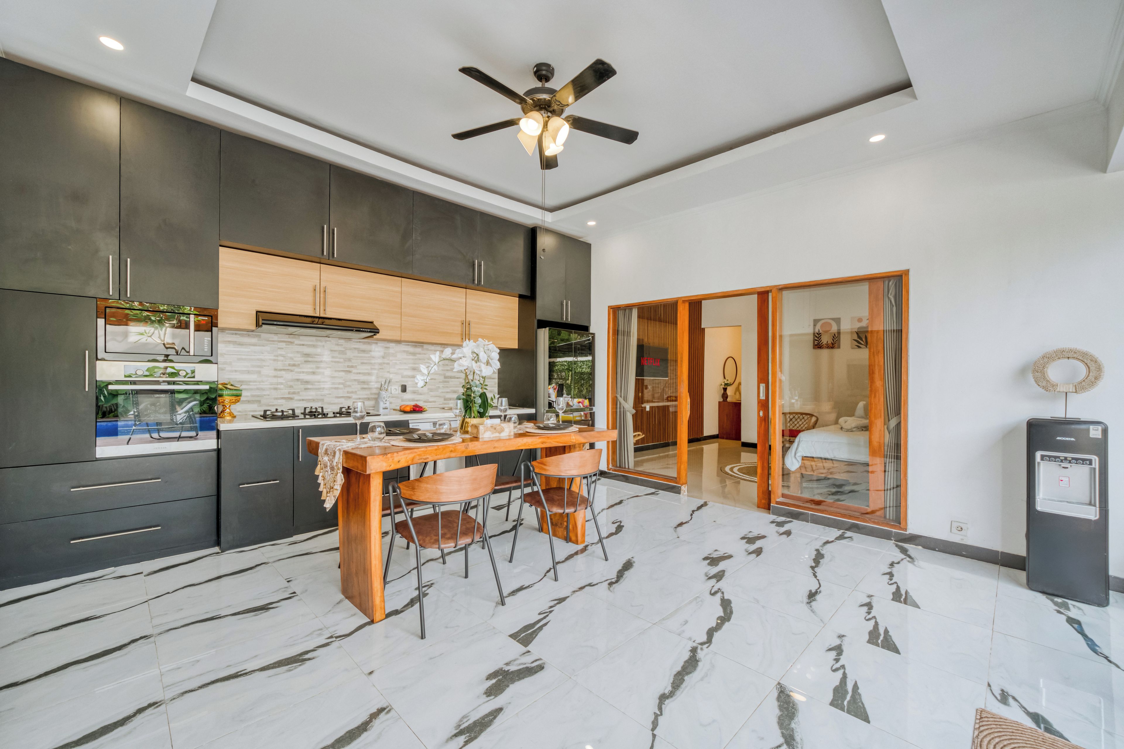 A modern kitchen with dark cabinets, a wooden island, and a ceiling fan.