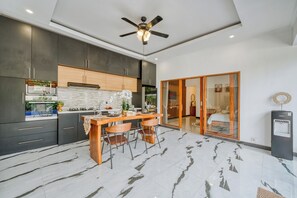 A modern kitchen with dark cabinets, a wooden island, and a ceiling fan. - Stylish 3BR Pool Villa in Canggu, Bali (Bali)
