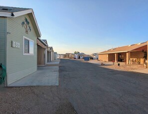 Une rue résidentielle bordée de maisons de plain-pied, avec un ciel dégagé et une route en gravier.
