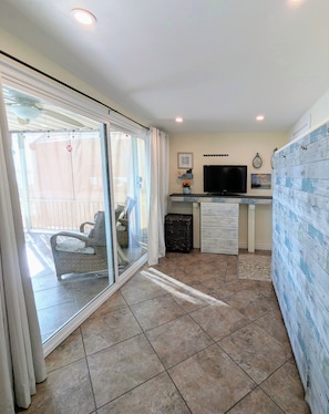 A room with a sliding glass door leading to an outdoor area, a flat-screen TV mounted on the wall, and a small cabinet with drawers. - Lakefront Home — Marina & Sunset Views! (Lake Havasu City)