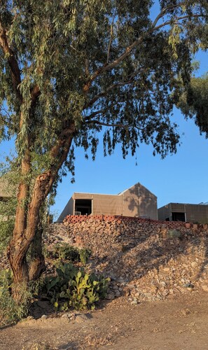 Ein Gebäude mit flachem Dach, umgeben von felsigem Gelände und vereinzelter Vegetation.