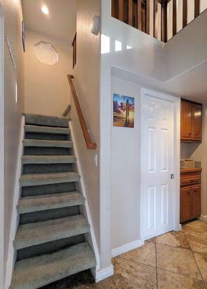 A staircase with carpeted steps leading to a landing, a white door with a painting, and wooden cabinets in the background. - Lakefront Home — Marina & Sunset Views! (Lake Havasu City)