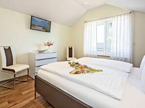 A hotel room with a bed, a desk, a chair, a window with curtains, and a painting on the wall. - Holiday Apartment With 1 Bedroom (Heringsdorf)