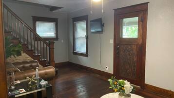 A living room with a staircase, wooden flooring, a ceiling fan, and a door with a window.
