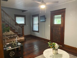 A living room with a staircase, wooden flooring, a ceiling fan, and a door with a window.